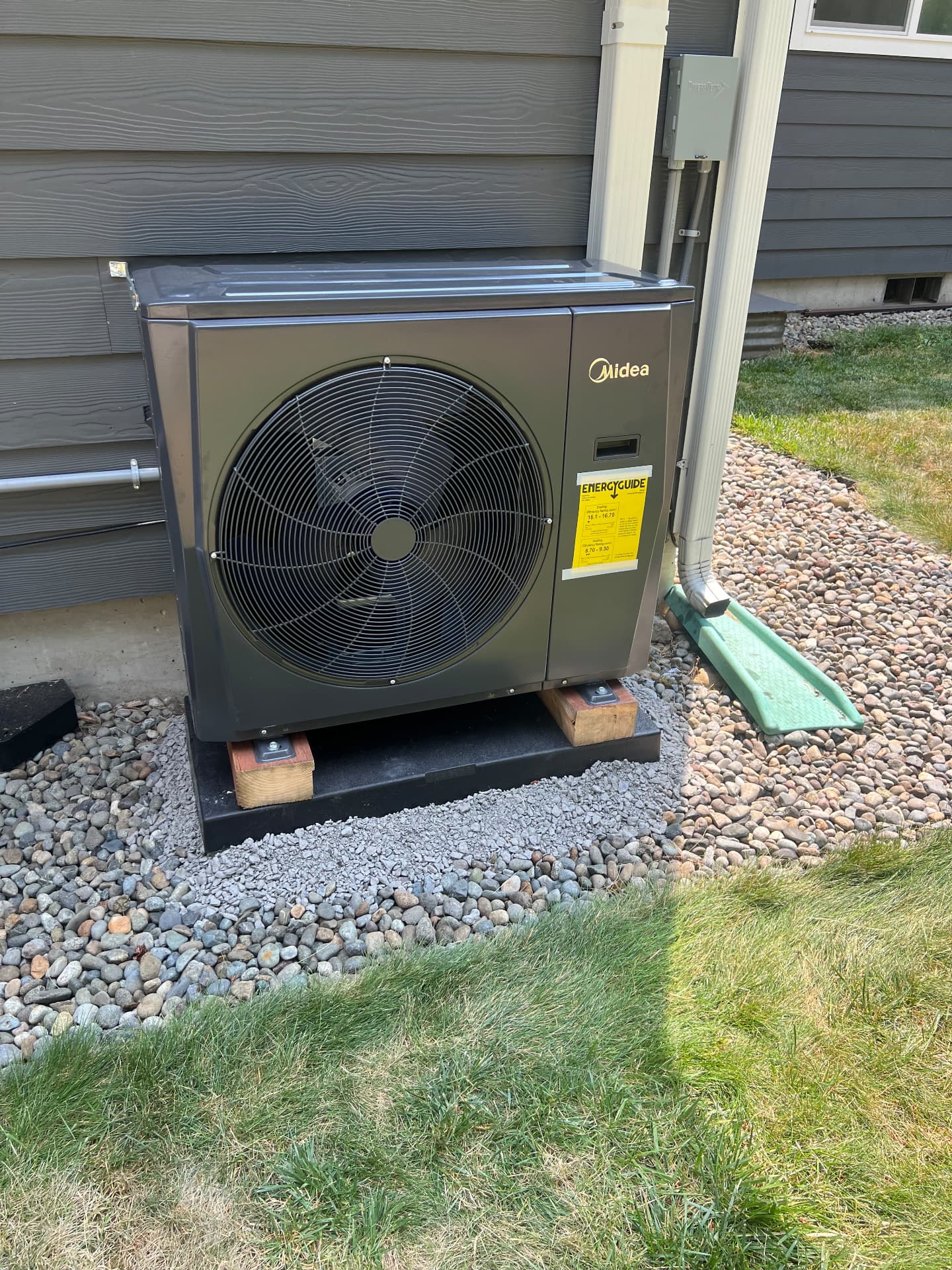 Midea heat pump installed on a pad beside a home